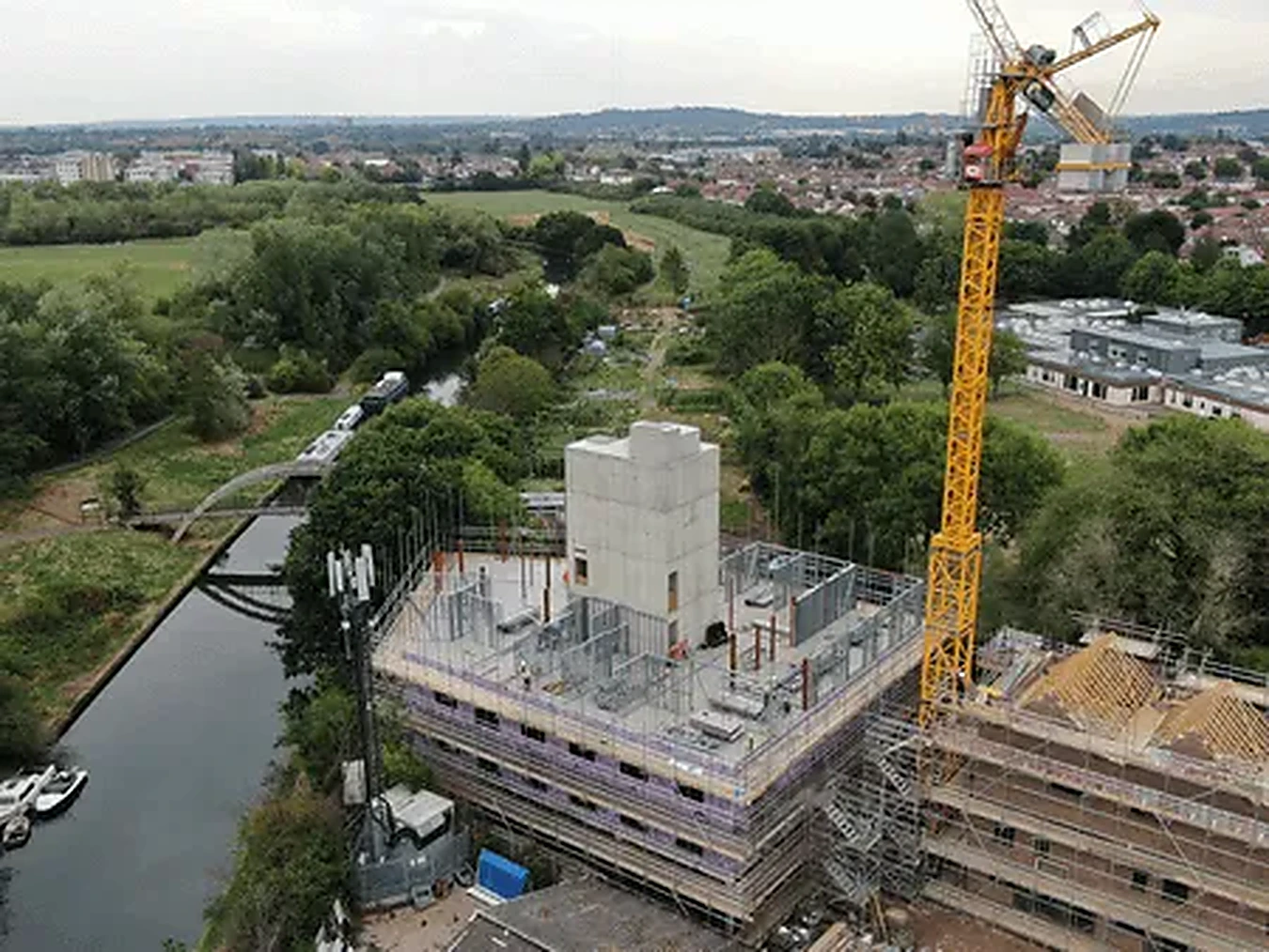 Scaffold hoist and staircase tower serving a multi-storey apartment block wrapped in scaffolding and debris netting
