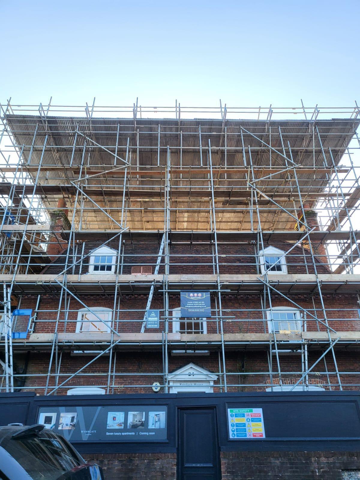 Brick building beneath a wide temporary roof scaffold with a loading level for materials