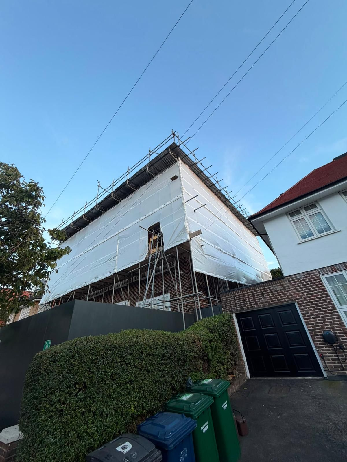 Sheeted temporary roof scaffold enclosing a residential construction project