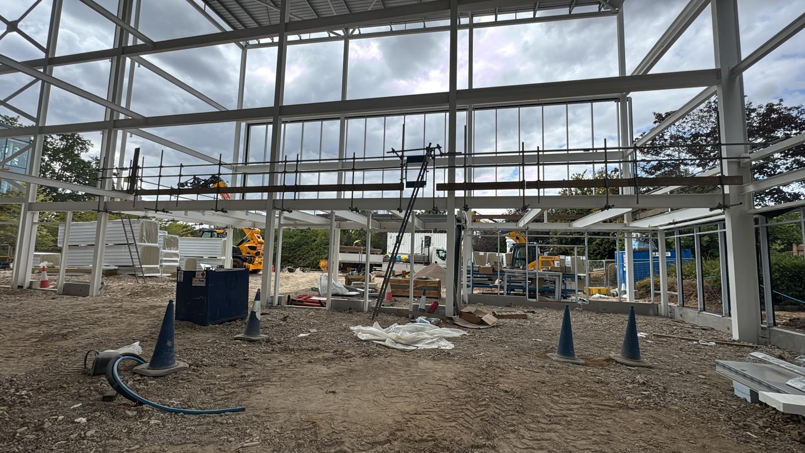 Scaffold tube and timber edge protection fitted to the open first floor edge of a steel frame commercial building