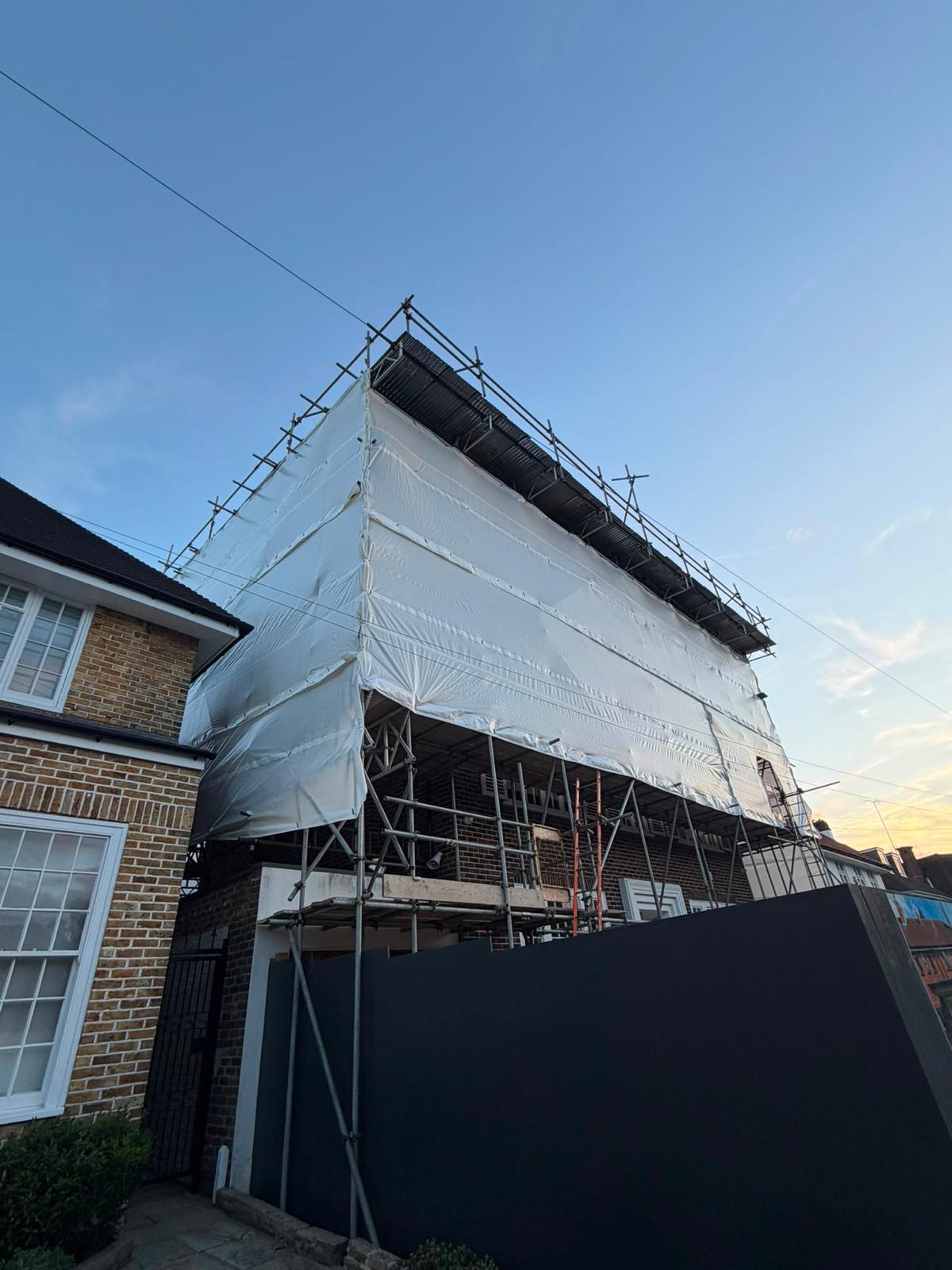 Scaffold and temporary roof beside a site hoarding with a protected loading area at street level