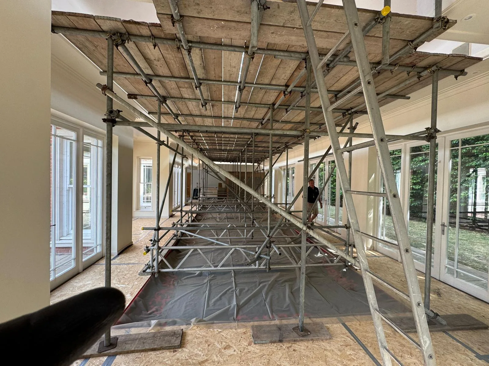 Birdcage scaffold forming a fully boarded working deck across a long interior room for ceiling access